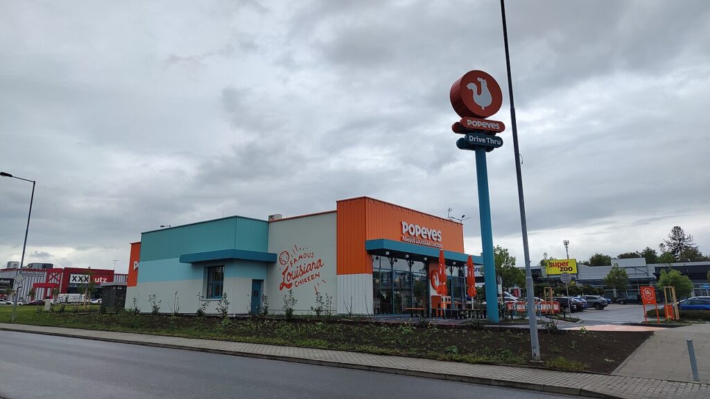 Budynek restauracji Popeyes z pylonem Drive Thru przy parkingu centrum handlowego